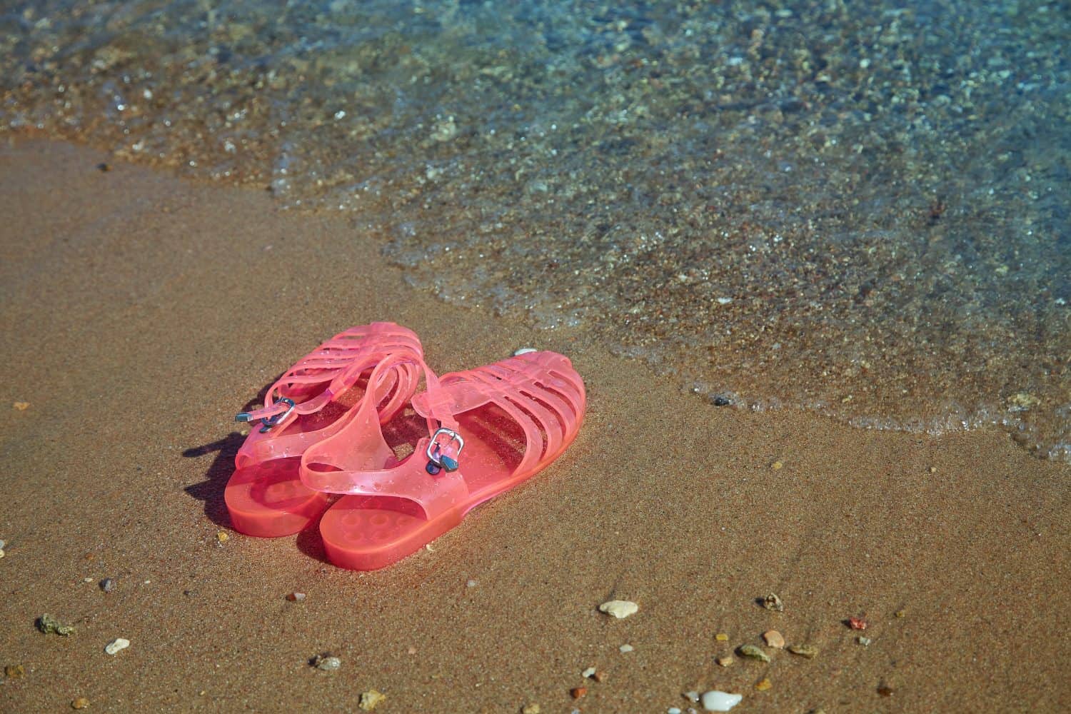 Pink Women's JELLY SANDALS on a sea shore. LADIES FLAT JELLIES SUMMER BEACH SHOES. Sand background