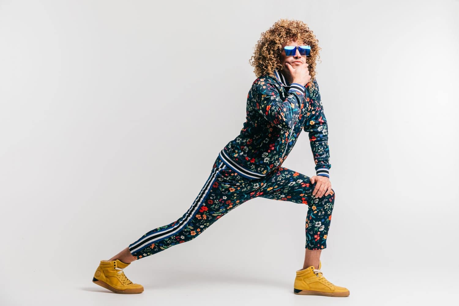 Adult positive smiling funky man with curly hair style in suglasses and vintage clothes posing on white studio background. Funny portrait of stylish male person. 80s fashion. Unusual eccentric guy