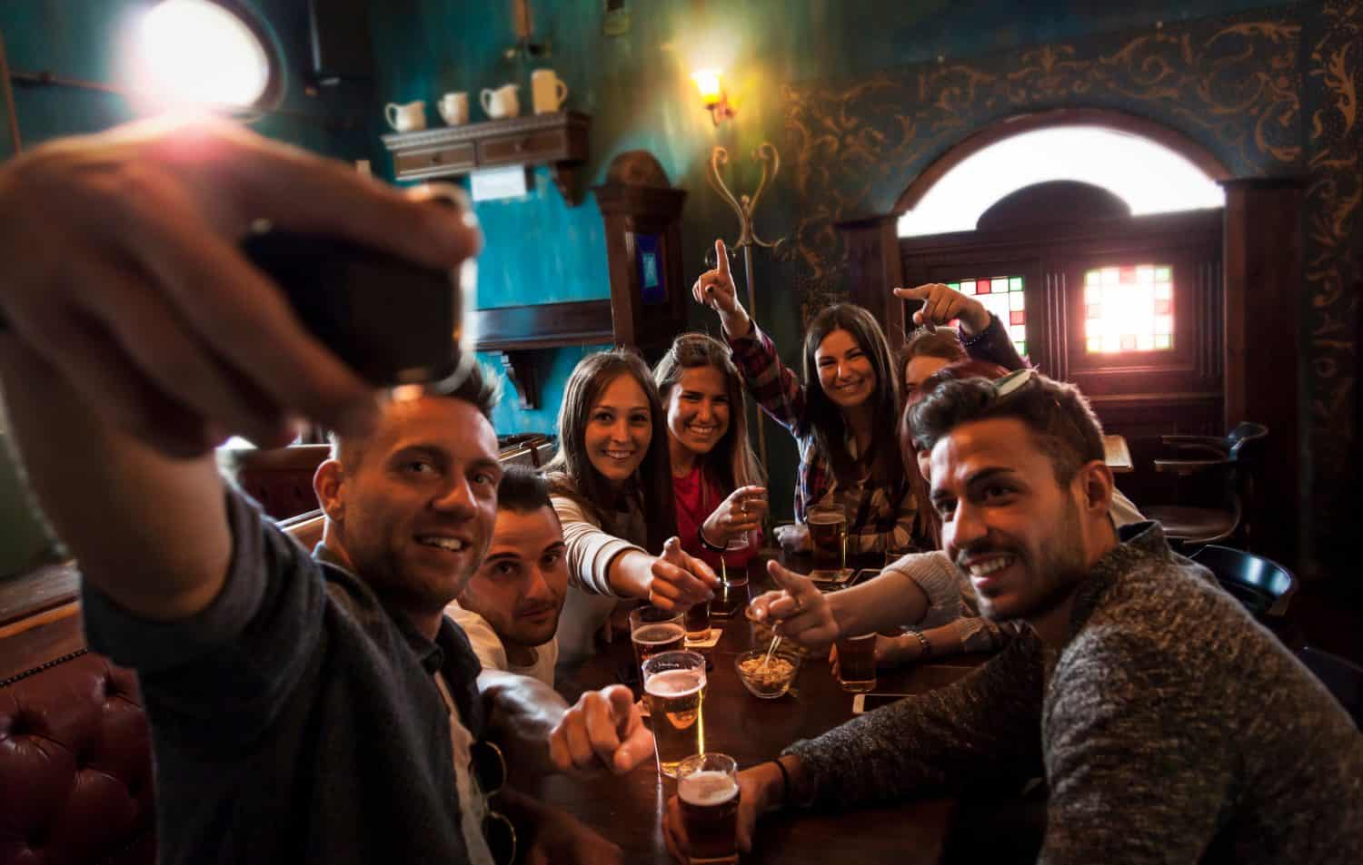 group of millennial people takes a selfie in a pub drinking beer and eating snacks