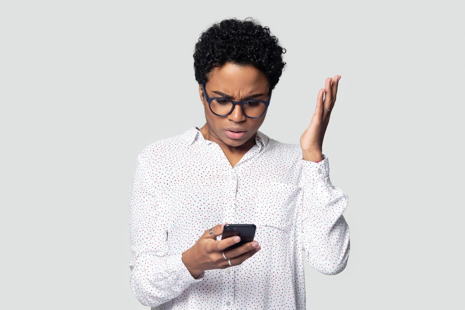 Confused african American millennial woman isolated on grey studio background hold smartphone have problem with gadget, frustrated biracial female experience cellphone malfunction or virus attack