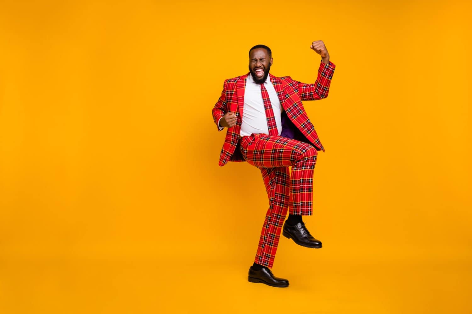 Full body photo of crazy ecstatic dark skin guy raise fists celebrate successful achieve good mood wear plaid red costume blazer pants footwear isolated bright yellow color background