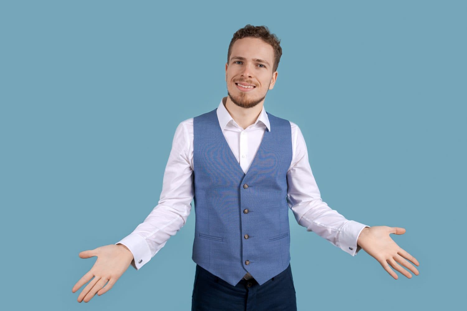 Portrait handsome excited man in business clothes smiling and showing hand gestures at the camera, isolated on blue background, young caucasian man with stubble on his face