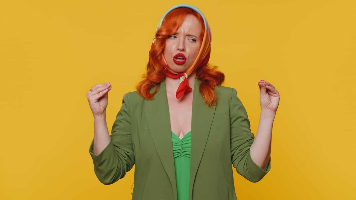 Gossips. Liars. Redhead young woman showing bla-bla-bla nonsense gesture with hands and rolling eyes, gossips, empty promises, blah concept. Adult ginger girl indoors isolated on yellow background