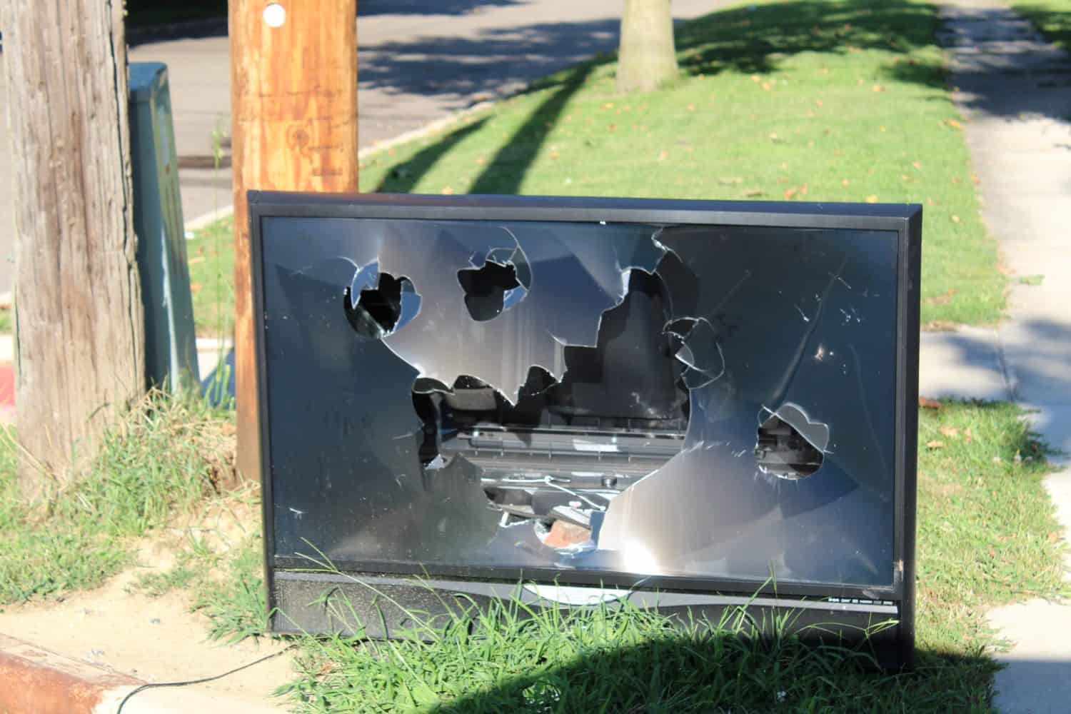 A discarded flat-screen television with a busted screen sits on a curb