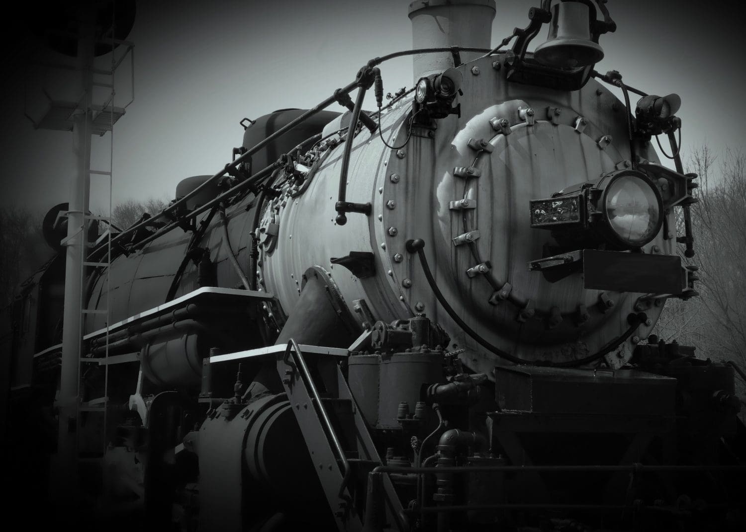 Black and white low angle front view of steel 1800s steam train engine next to railroad signal
