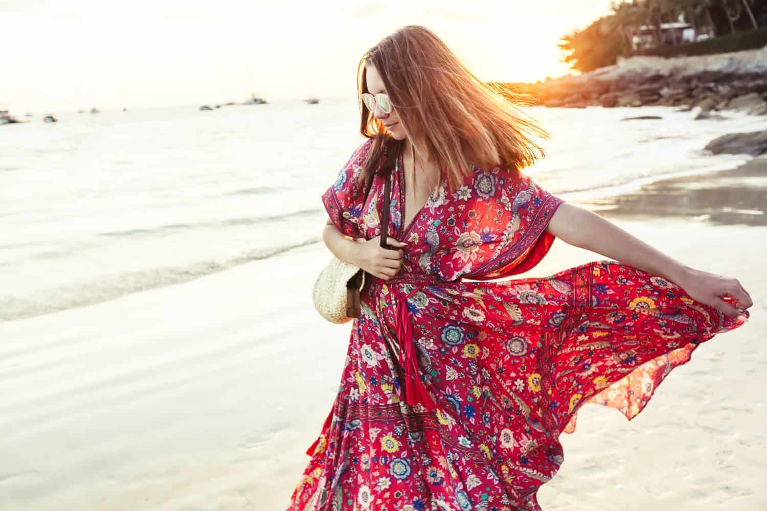 Young beautiful girl wearing boho maxi dress walking on sand. Summer fashion clothes for the beach.