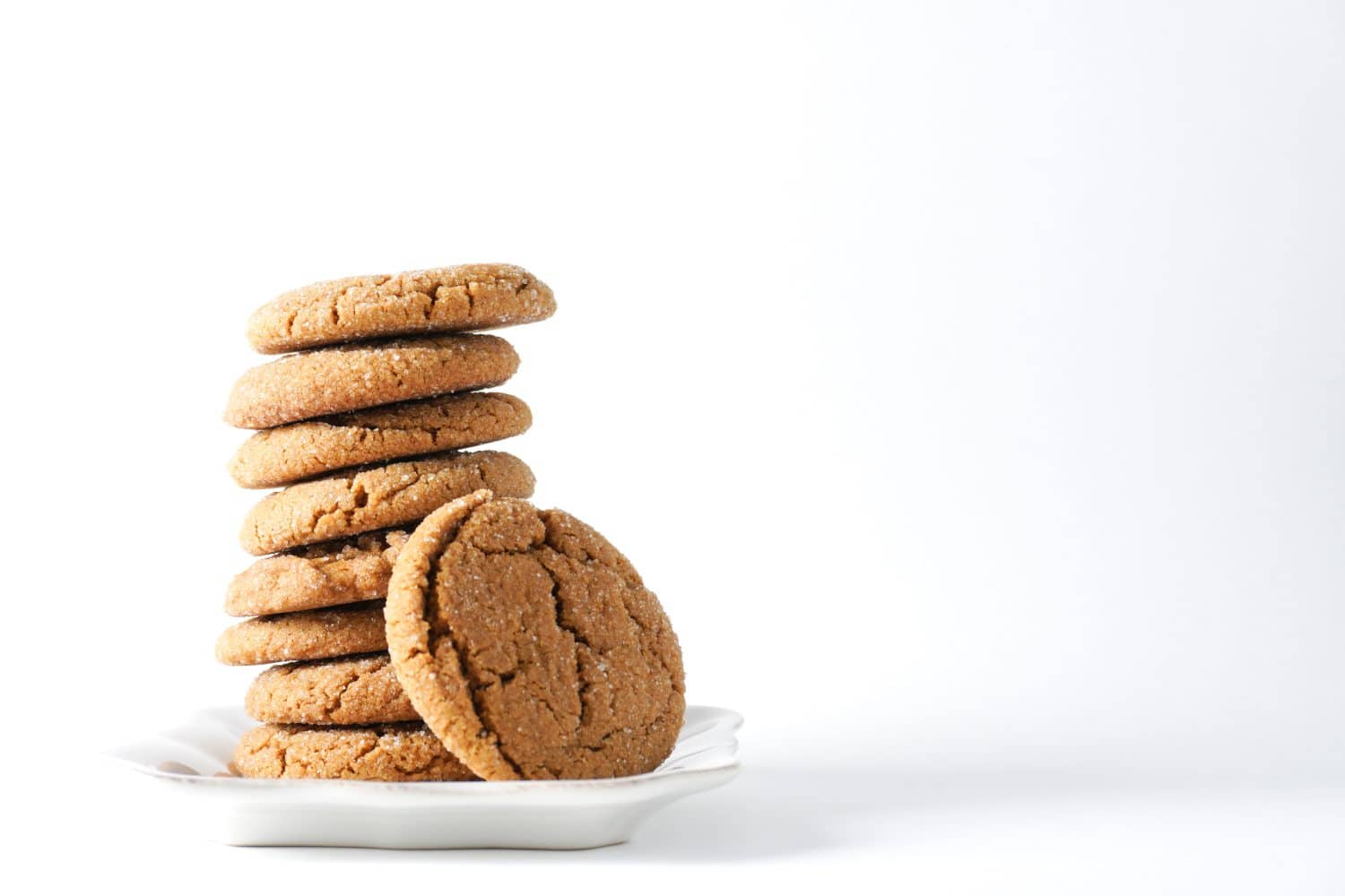 A gingerbread cookie leans on a stack on cookies on a white plate isolated on a white background; copy space on right