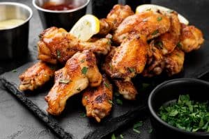 Baked chicken wings served with different sauces and lemon. Black background