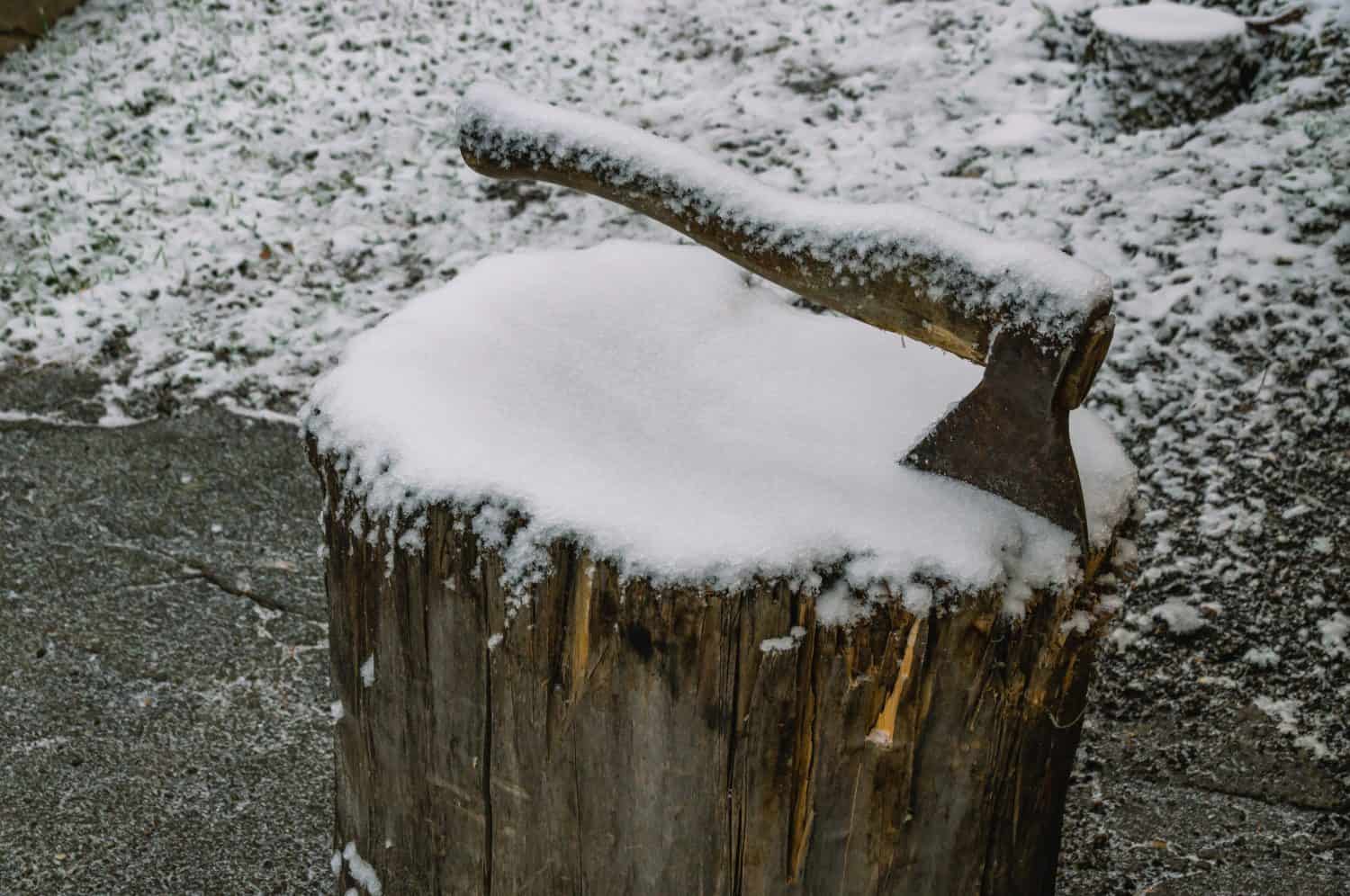 A snow-covered axe on a wooden block. Harvesting firewood for heating in the village in winter. Life in the countryside in winter.