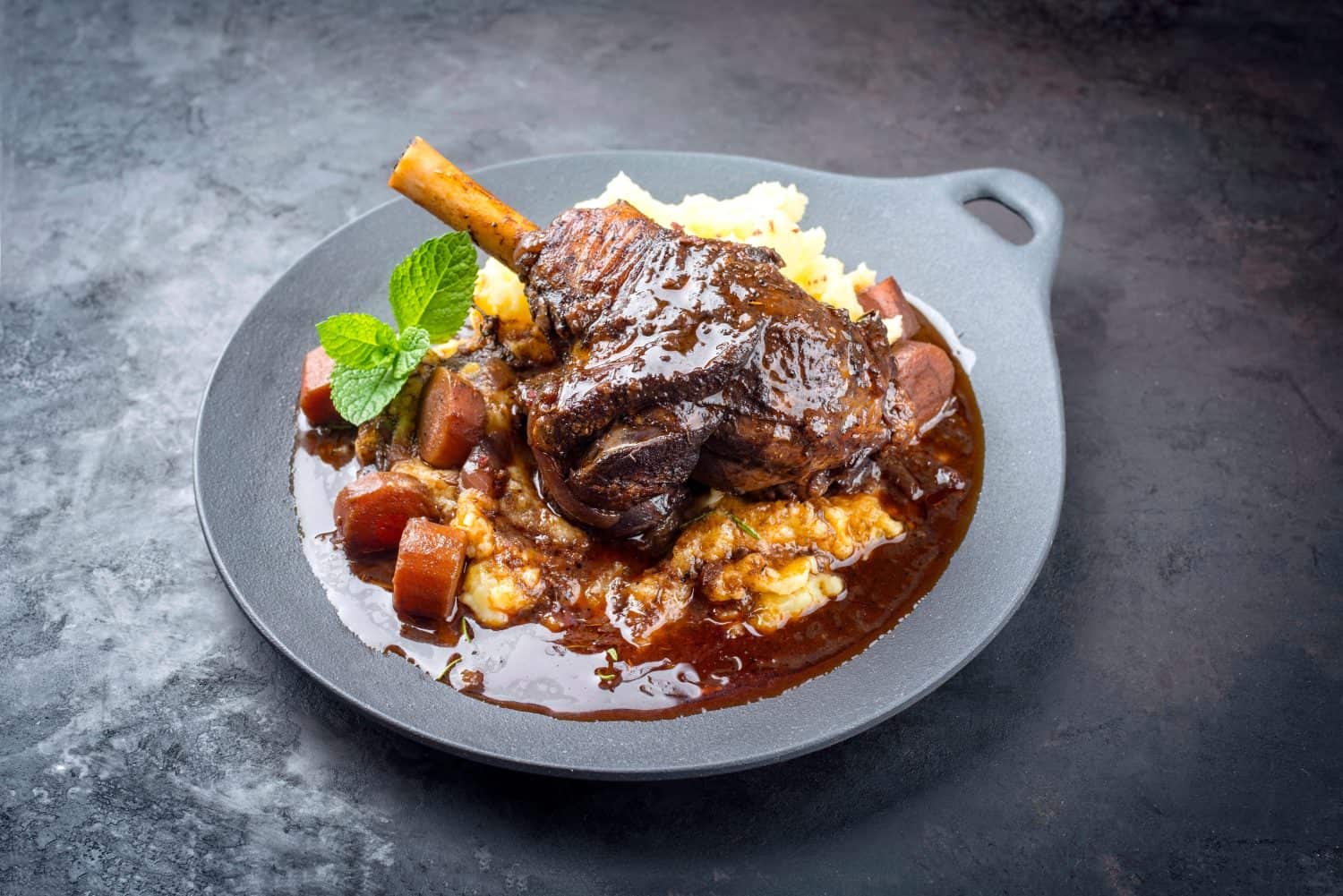 Modern style traditional braised slow cooked lamb shank in red wine sauce with shallots and mashed potatoes offered as top view in a design cast iron plate with copy space