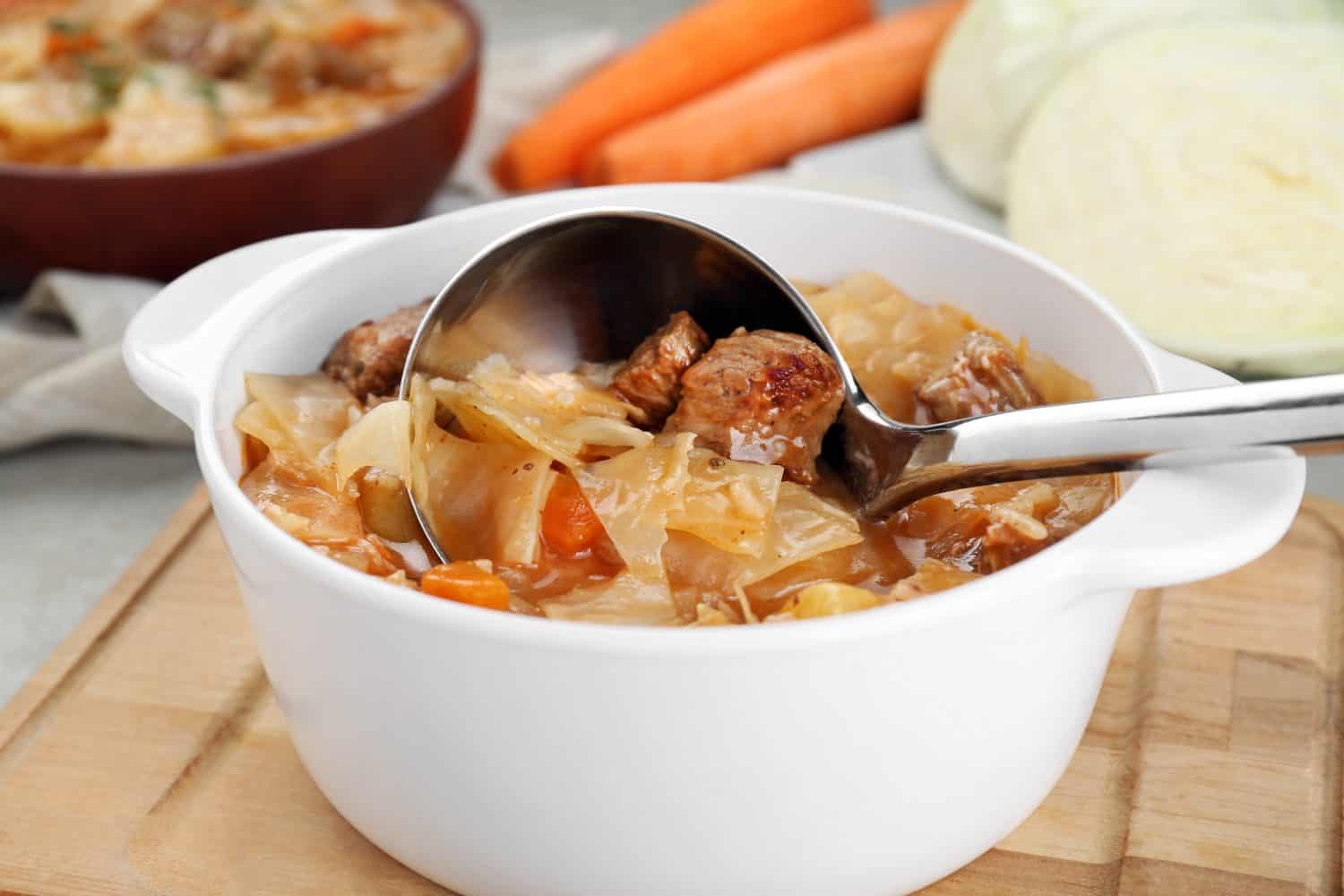 Tasty cabbage soup with meat and carrot on table, closeup