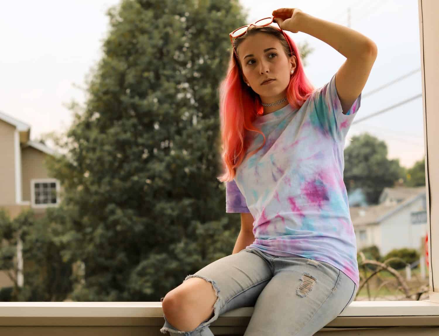 Young Pink Haired Woman Taking her Sunglasses Off in a Tie Dye Tee Shirt