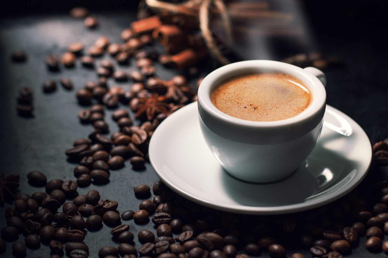 Fresh tasty espresso cup of hot coffee with coffee beans on dark background