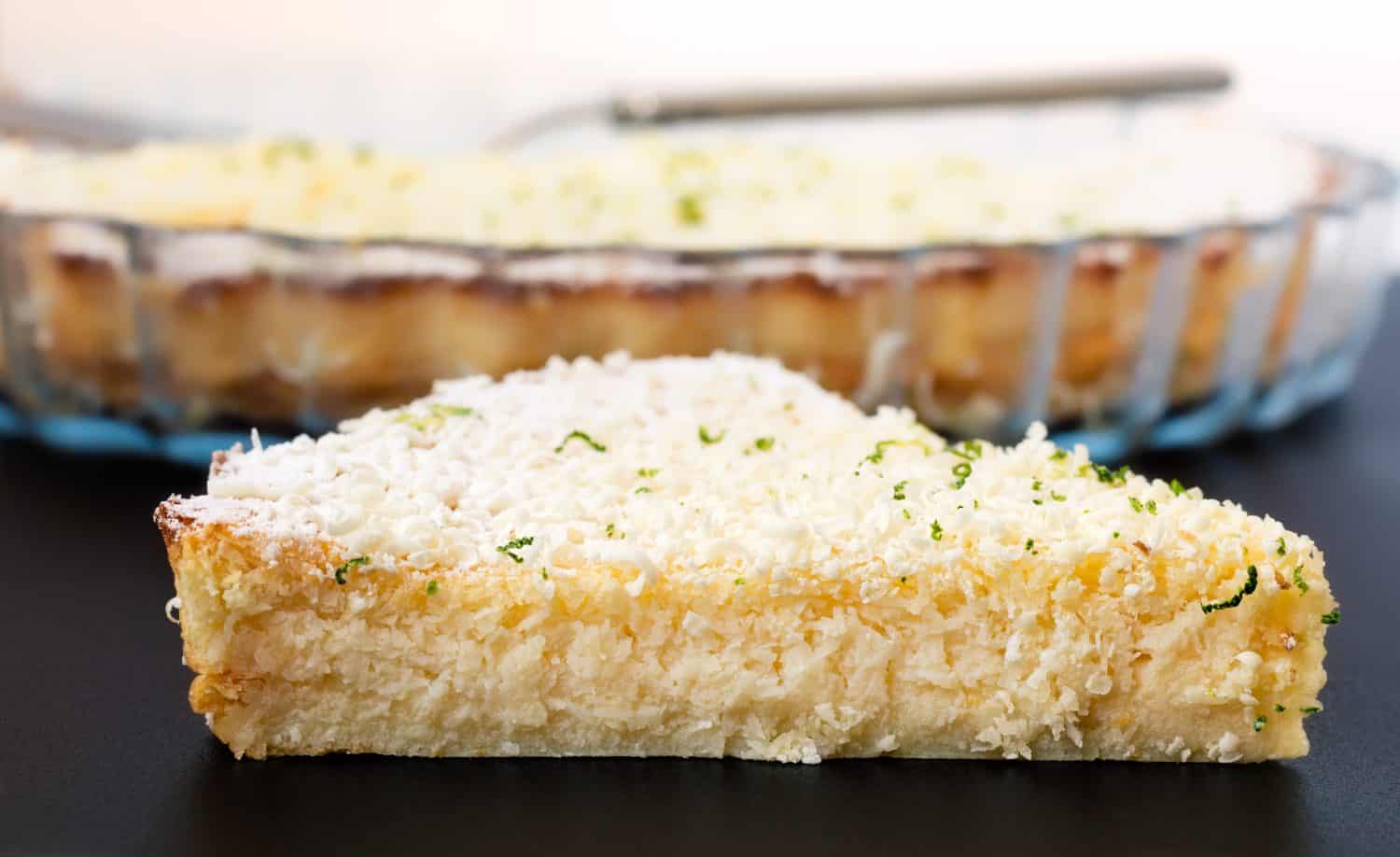 Lemon, lime, coconut impossible pie with white chocolate shavings slice with baking dish in the background