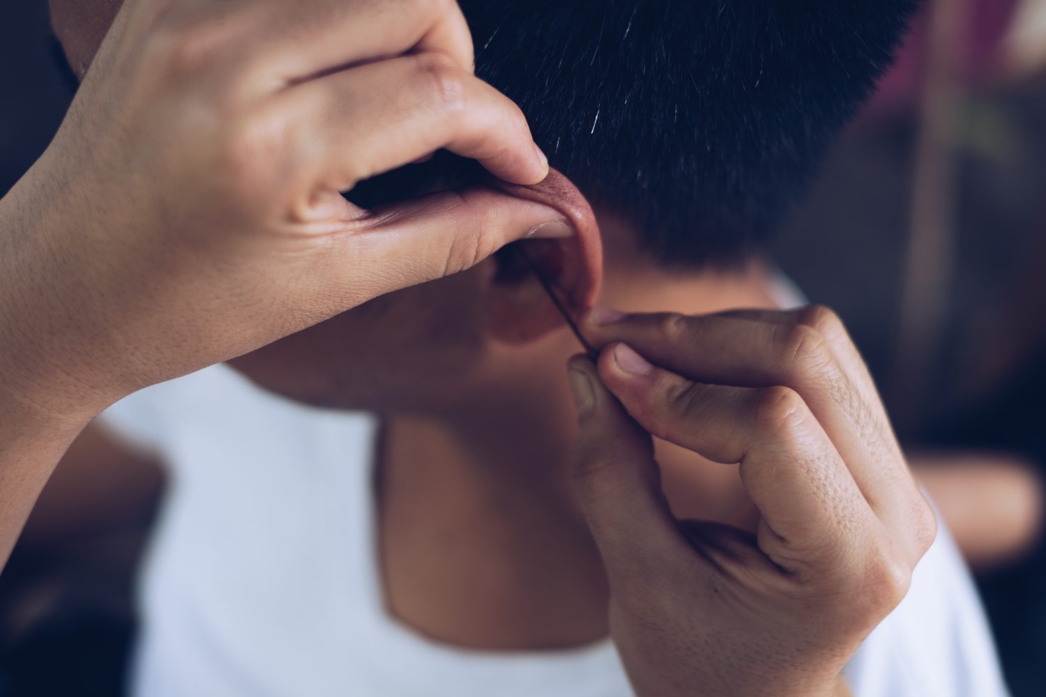 Closeup of hands manually cleaning a man's left ear of earwax using an ear pick. Selective focus.