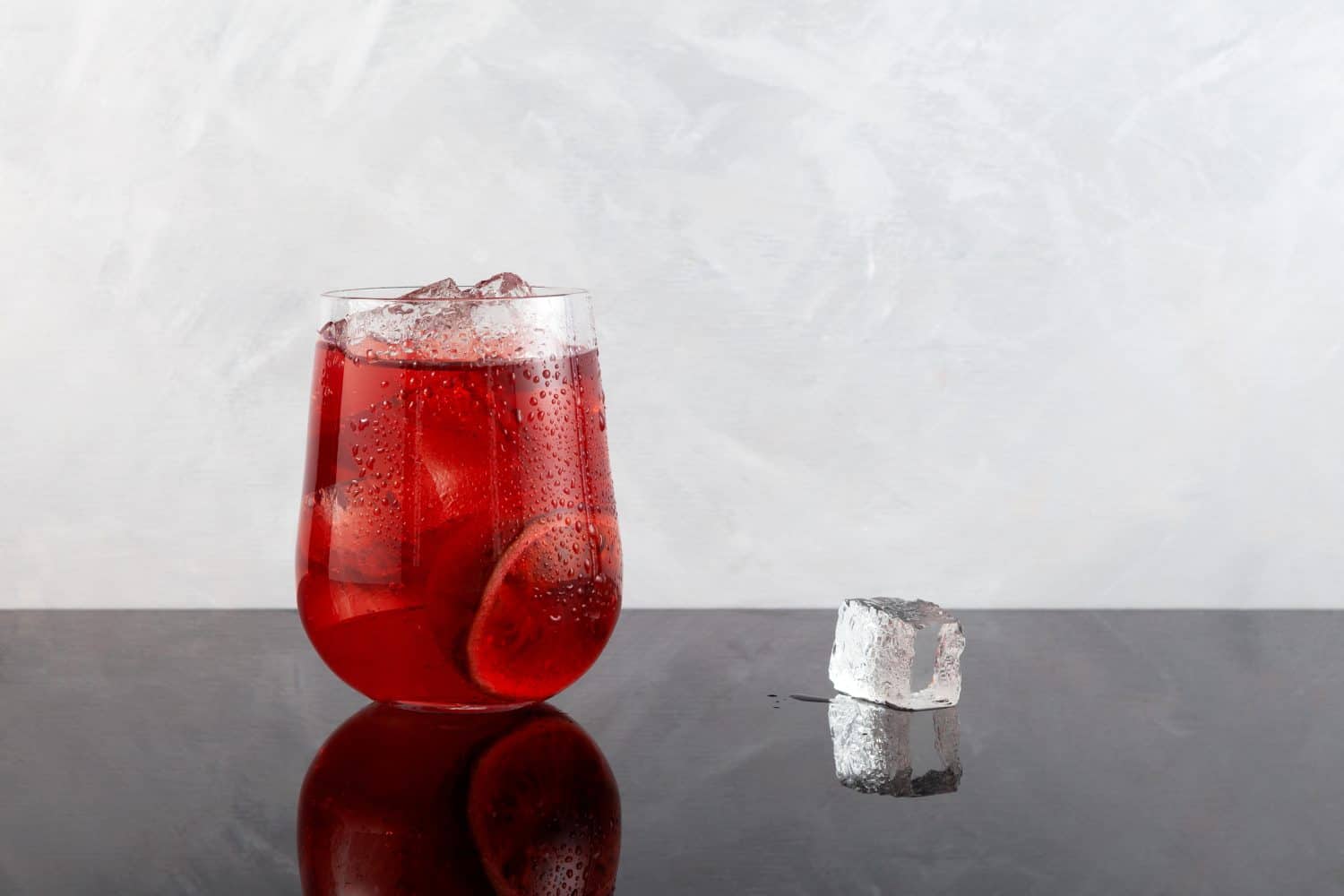 Red refreshing drink with ice or fruit iced tea. Lemonade with hibiscus and passion fruit. Grey background, copy space.