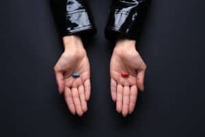 Hands with blue and red pills on dark background. Concept of choice