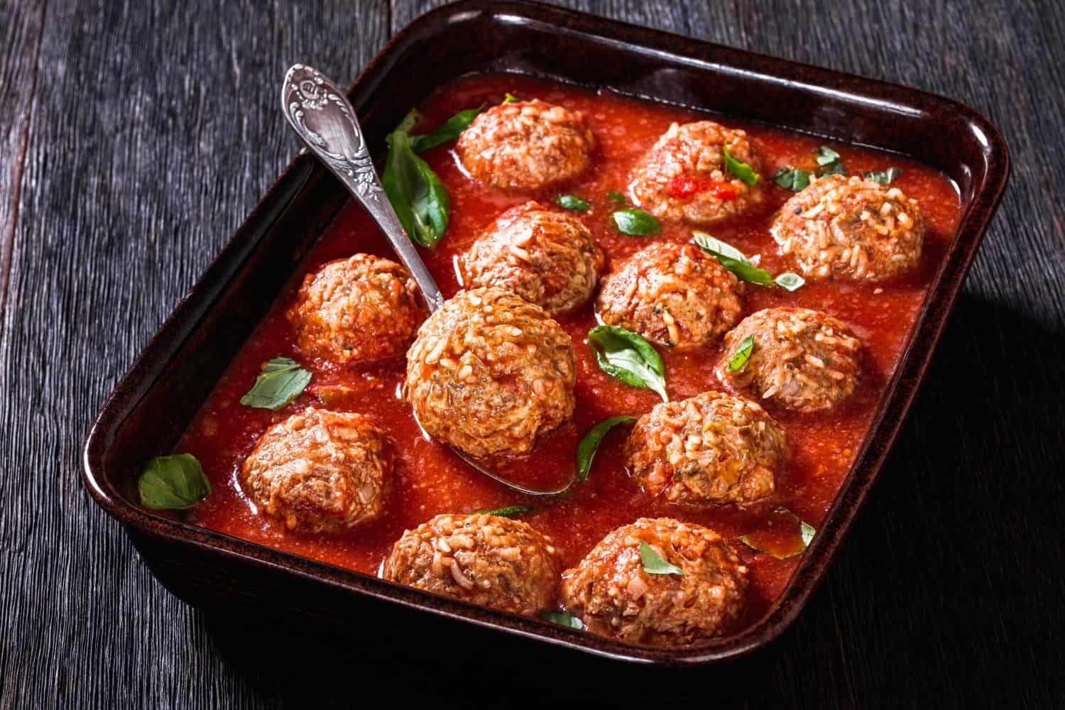 Italian Porcupine Balls, ground beef and rice meatballs in tomato sauce in rustic baking dish on dark wooden table, horizontal view, close-up