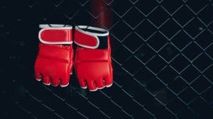 Red Gloves for MMA Boxers fighter hang on ring octagon black wall. Concept sport banner.