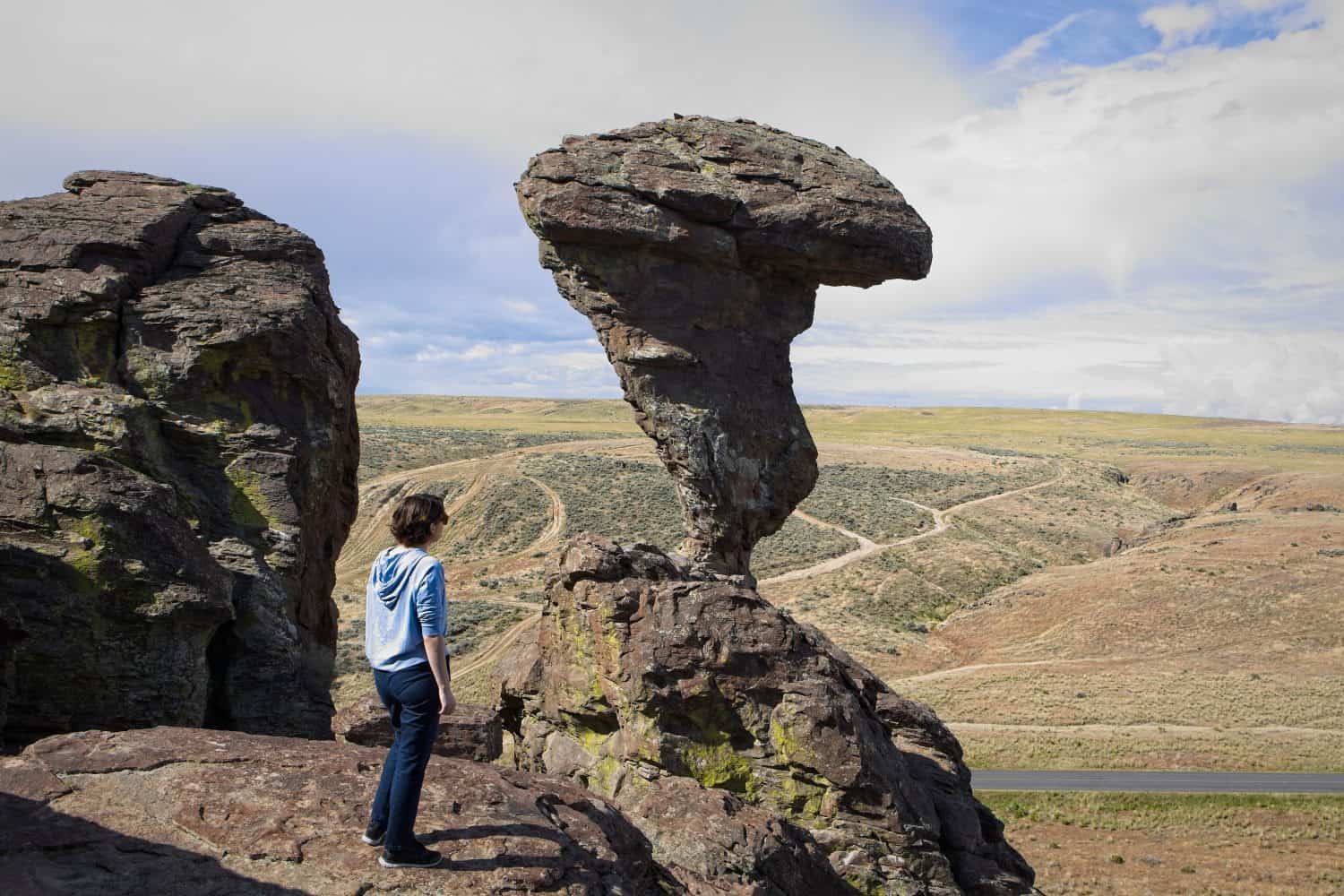 A young woman stands on a rock ledge looking at the famous Balanced Rock near Buhl, Idaho.