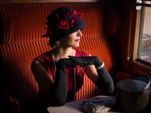 Attractive 1920s woman in red flapper dress and cloche hat posing in the 1927 first class interior of an authentic steam train