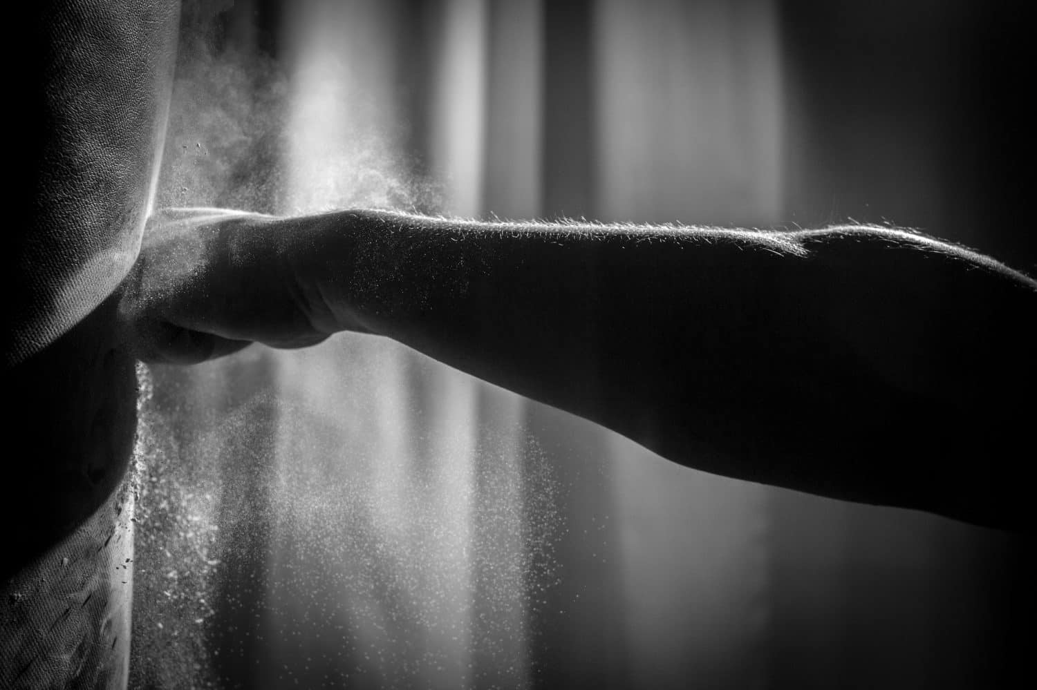 Shadowy, Black & White Close Up Action Photo of a Bare Knuckle Fist Hitting a Punching Bag with an Explosion of Dust