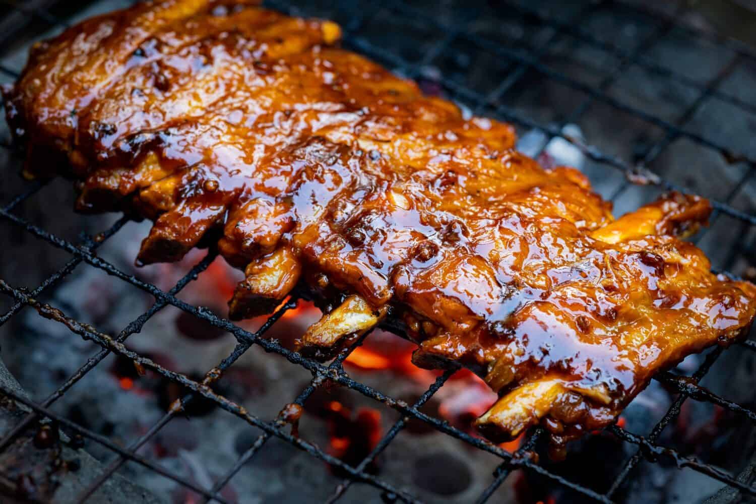 Pork ribs being grilled on smoldering charcoal