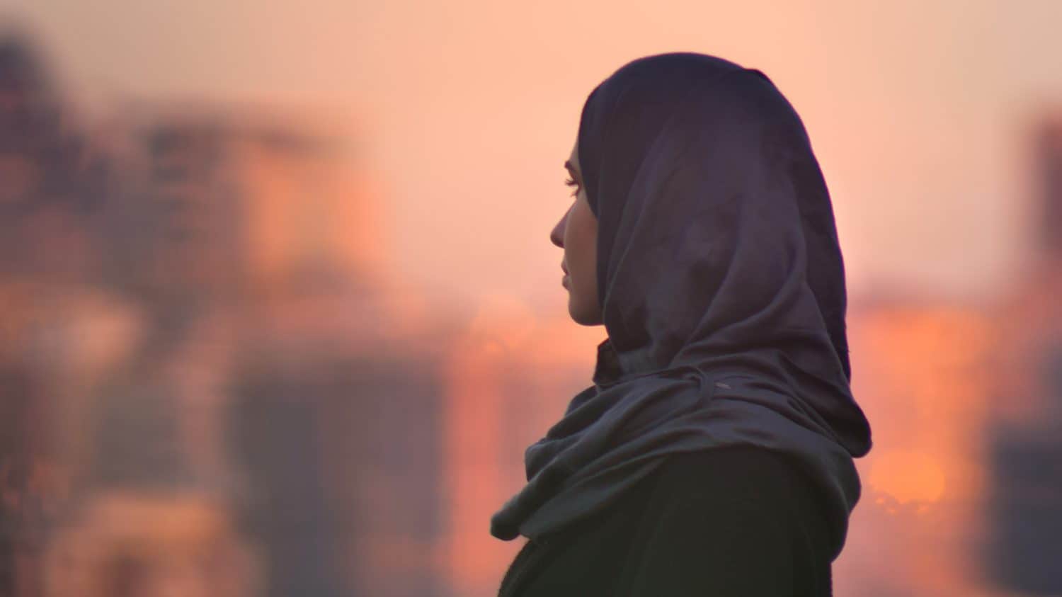 Closeup portrait of young pretty female in hijab looking forward with urban setting and shining buildings on the background