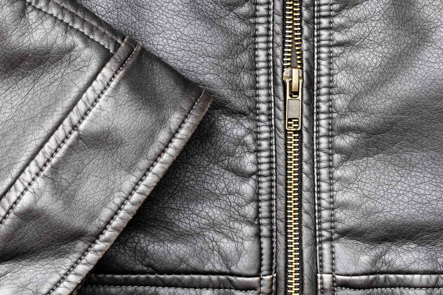 Close up of black stylish and fashion PU leather biker jacket texture with the textured surface, neat sewing seams, and vintage copper-plated zipper with elements, isolated, from above, background.