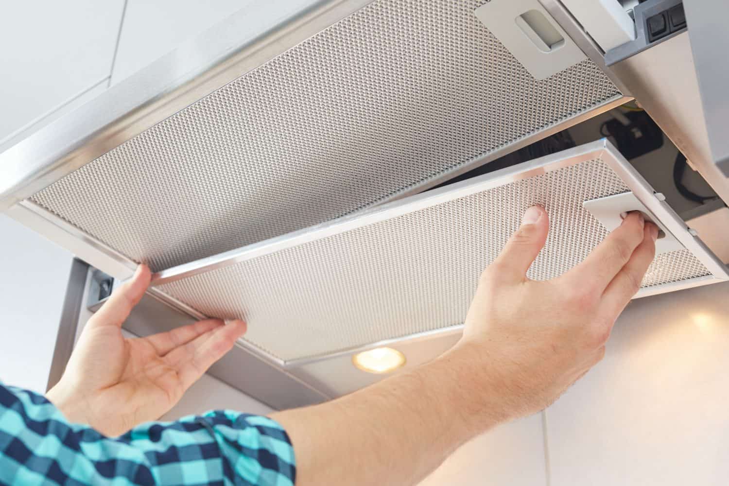 Removing a filter from cooker hood for cleaning or service. Replacing filter in kitchen hood. Modern kitchen fan or range hood.
