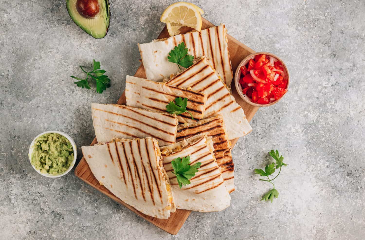 Grilled quesadillas on wooden board and with salsa and guacamole on stone background. Mexican cuisine concept Quesadilla wrap with chicken and corn. Top view