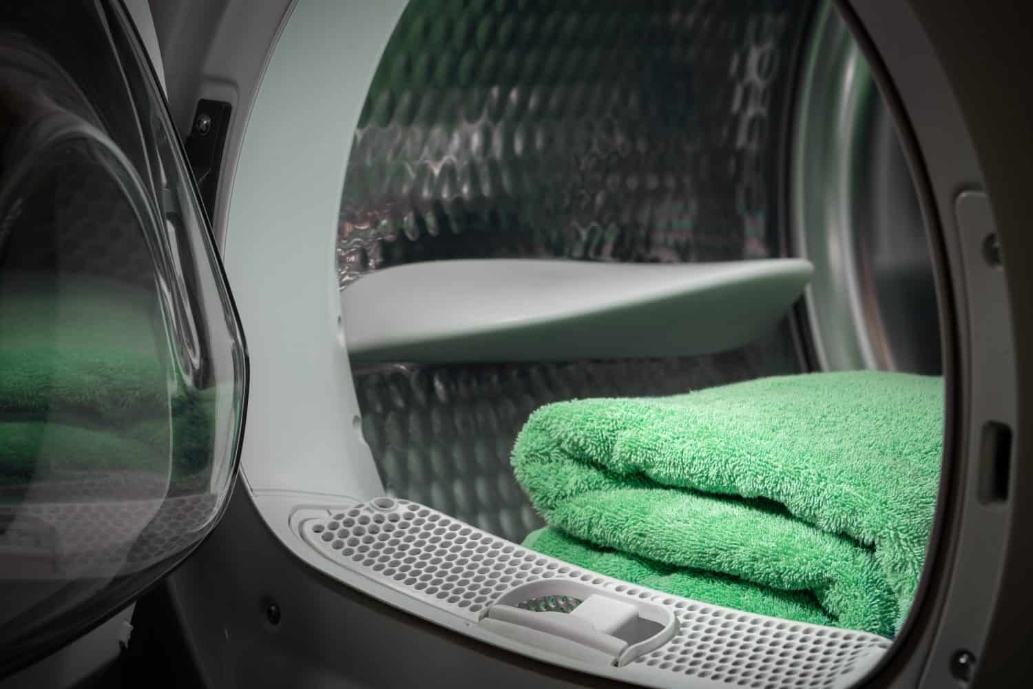 View of the tumble dryer or washing machine with the door open and a green towel inside