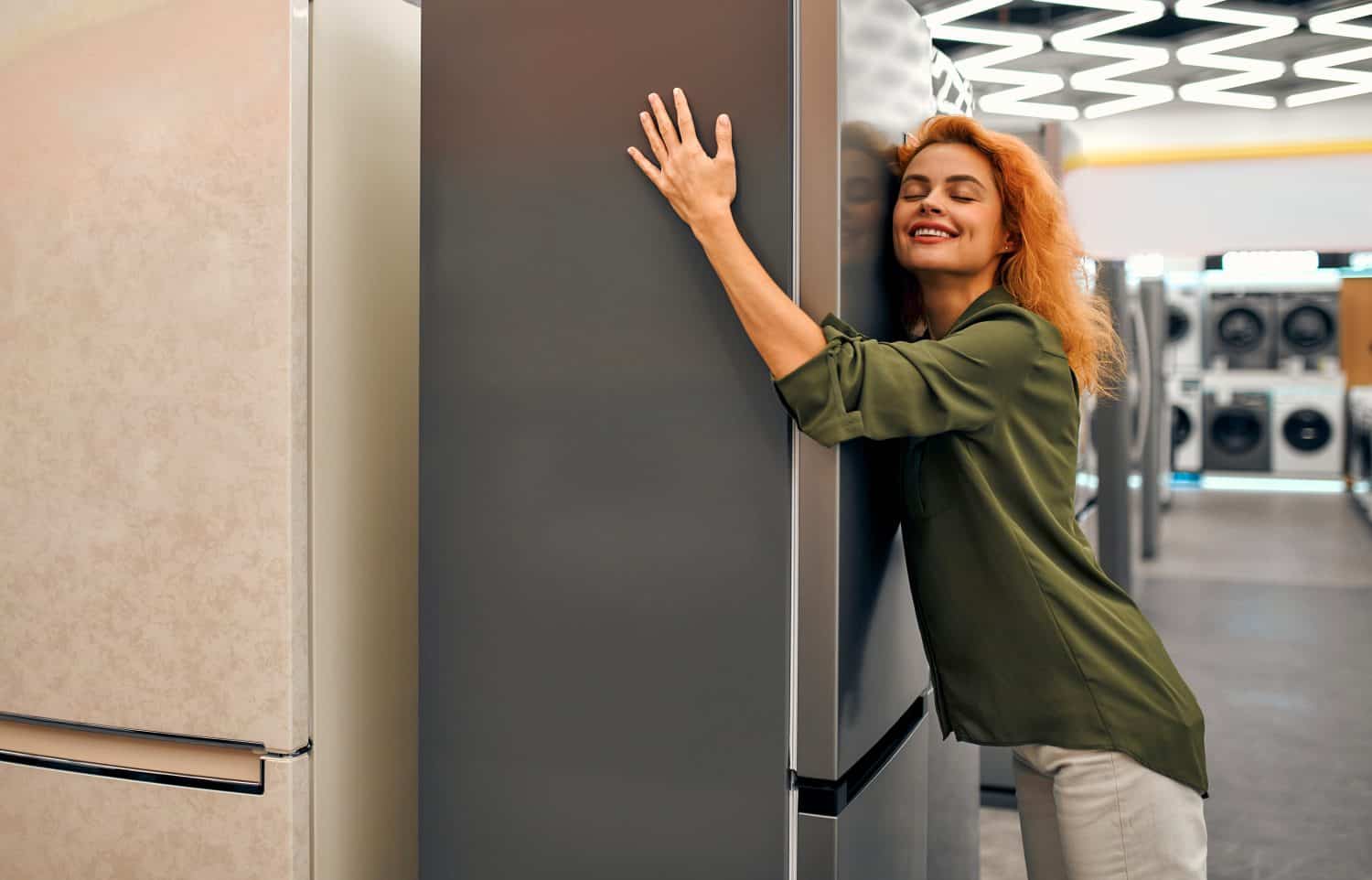 Woman hugging a refrigerator in a home appliances and electronics store. Buying a new refrigerator.