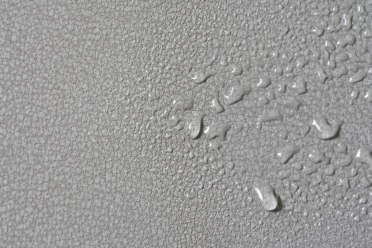 Gray water-repellent fabric for furniture or clothing, with moisture drops. Artificial surface. Modern nano-leather or eco-leather. Textured background or backdrop. Selective focus. Close-up. Macro.