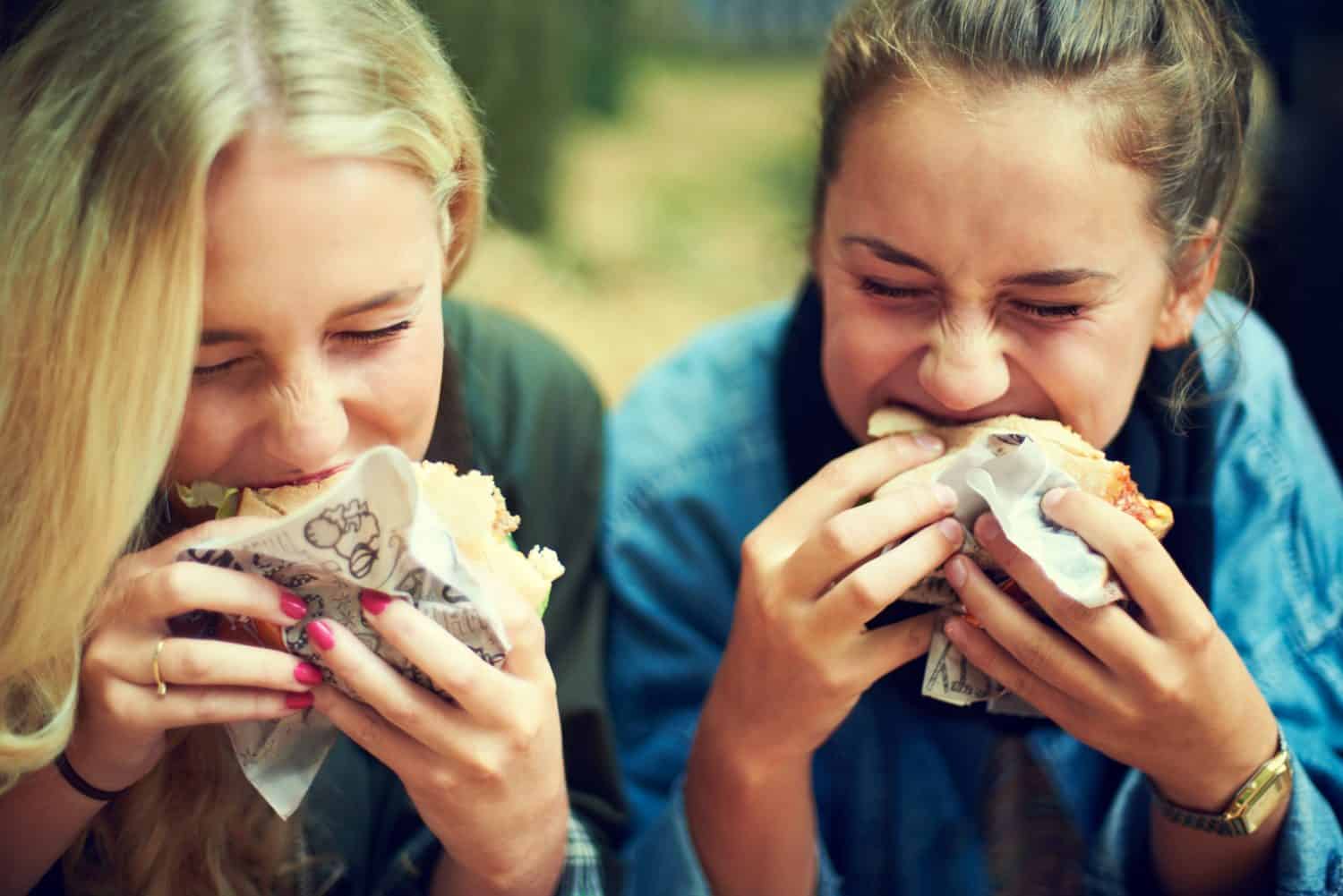 Got the munchies. Shot of two young women eating at an outdoor festival.