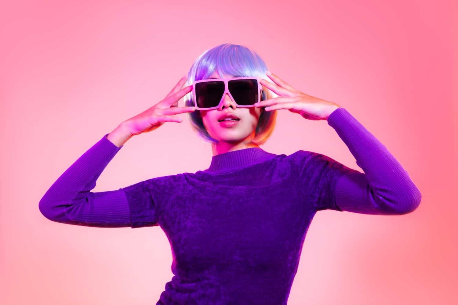 Young asian woman short blue milinium hairstyle wearing pink sunglasses posing on the red pastel and neon color background.