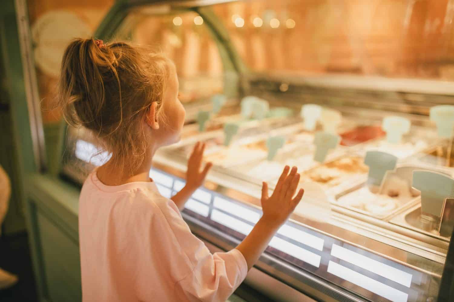 Cute little girl standing near ice-cream shop, choosing ice-cream.