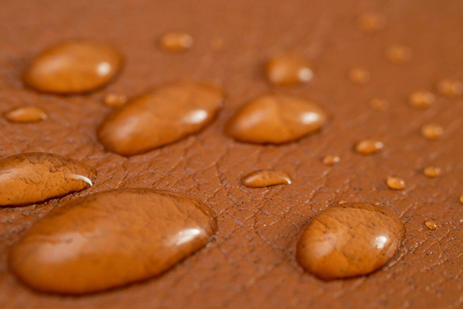 Round water drops on brown leather texture, side view, soft focus macro pattern