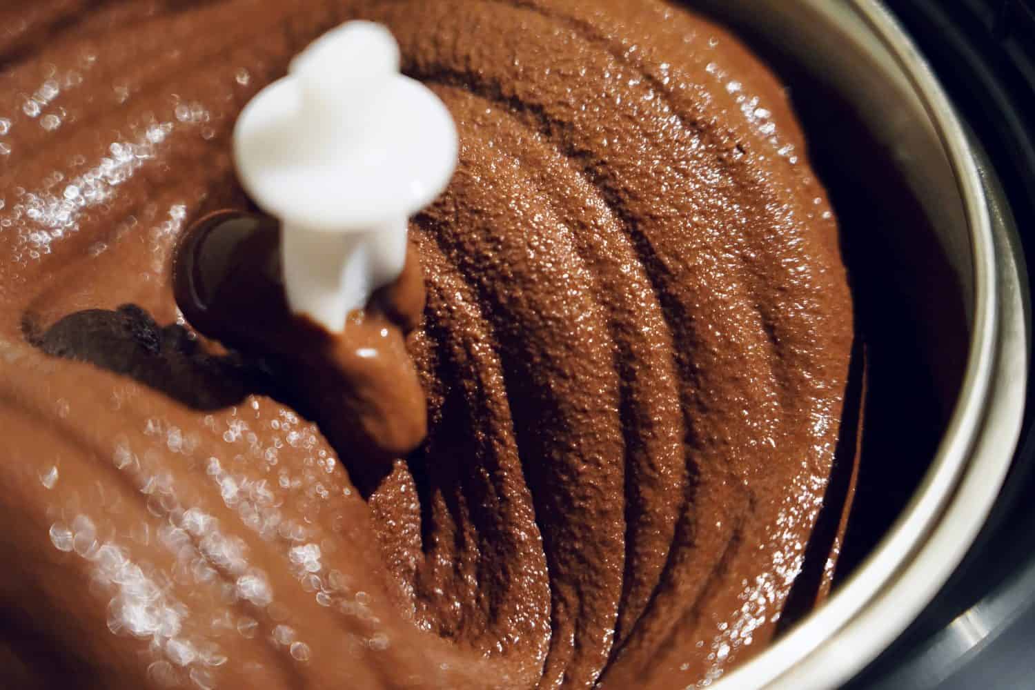 Freshly made chocolate gelato ice cream shining in an aluminum bucket of a churning machine.