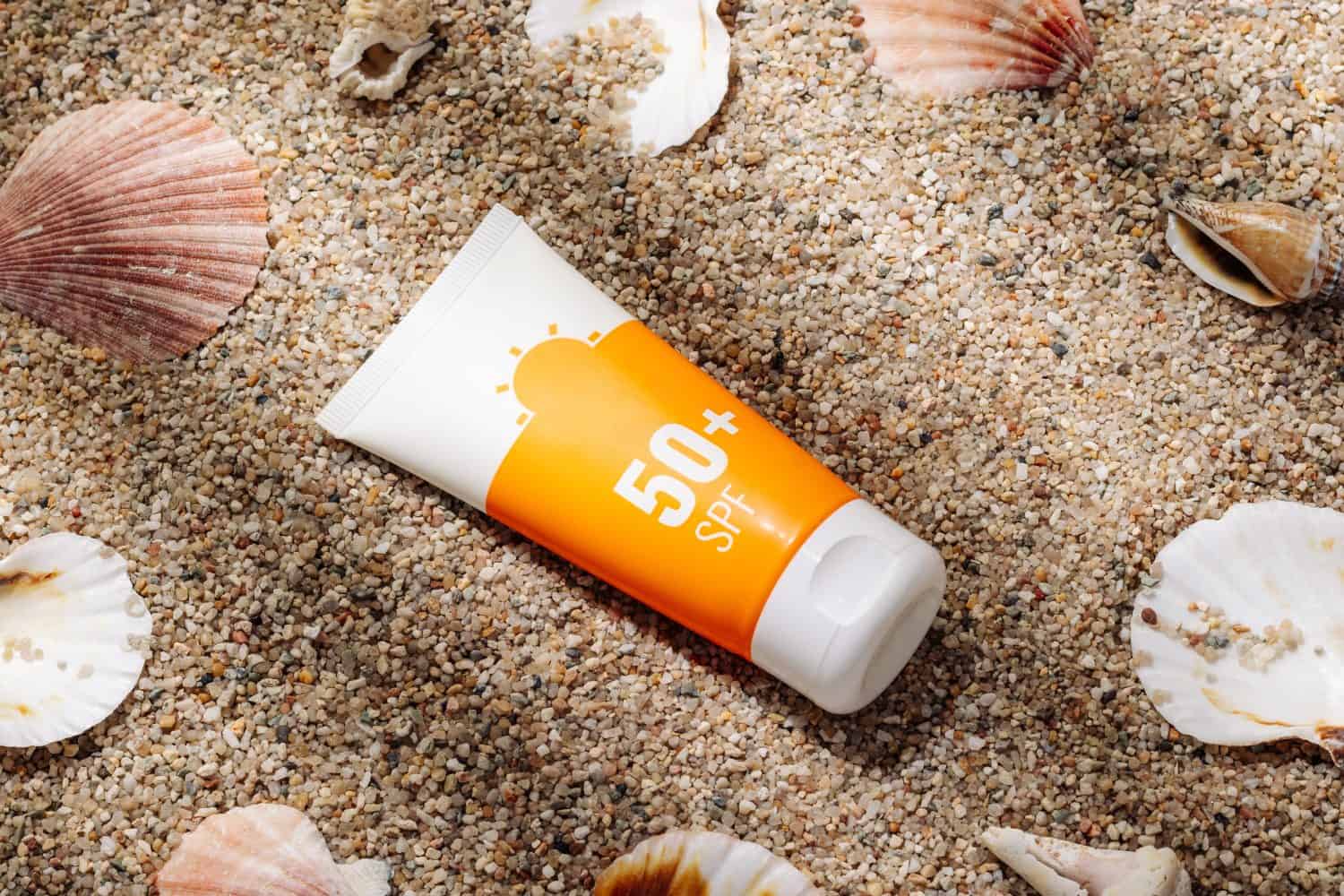 Orange tube of sunscreen on sandy beach top view