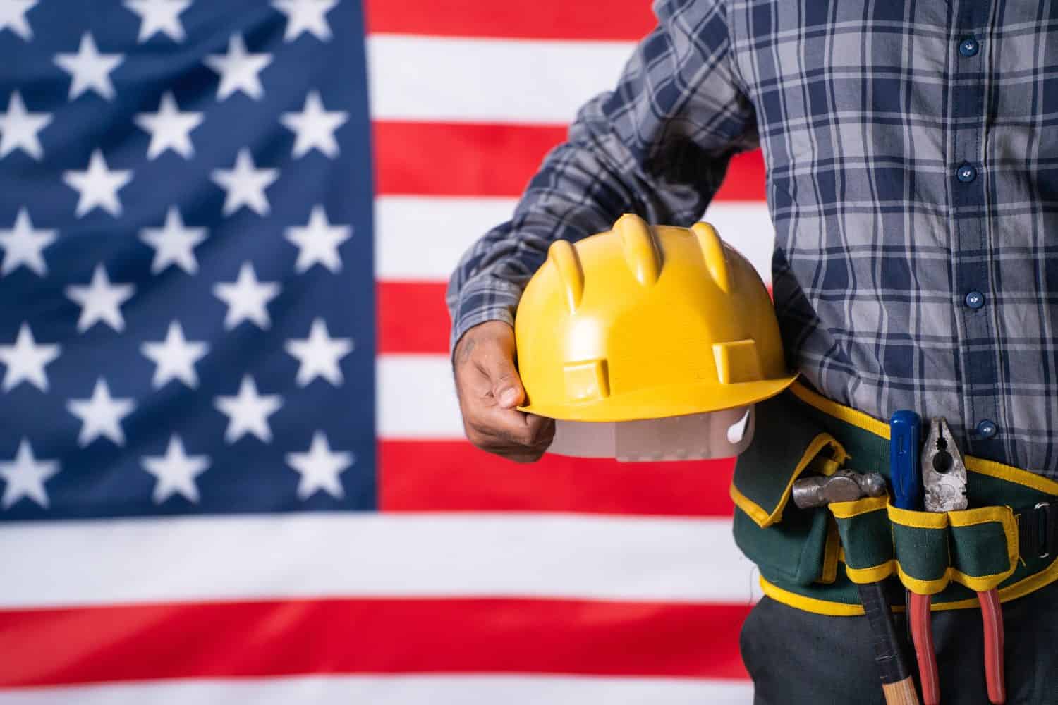Close up shot of labour with tools or equipment by holding helmet in hand in front of USA flag - concept of maintence service, labour day and employment.