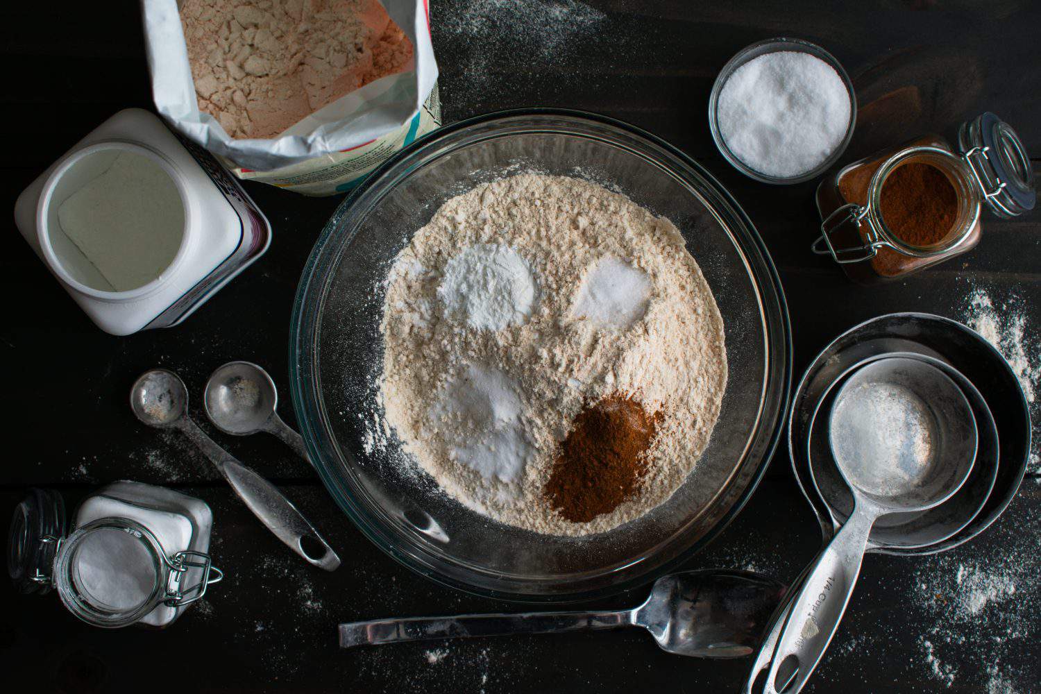 Mixing Dry Ingredients for Baked Apple Cider Donuts: Whole-wheat pastry flour in a glass mixing bowl surrounded by kitchen tools and ingredients