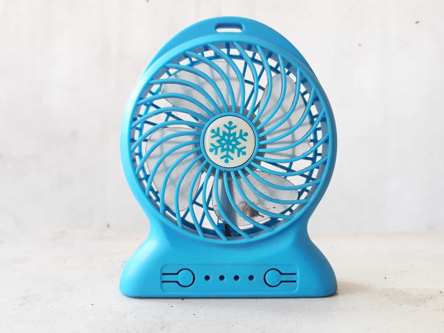 A dirty blue mini portable fan that has not been cleaned, on a white background.