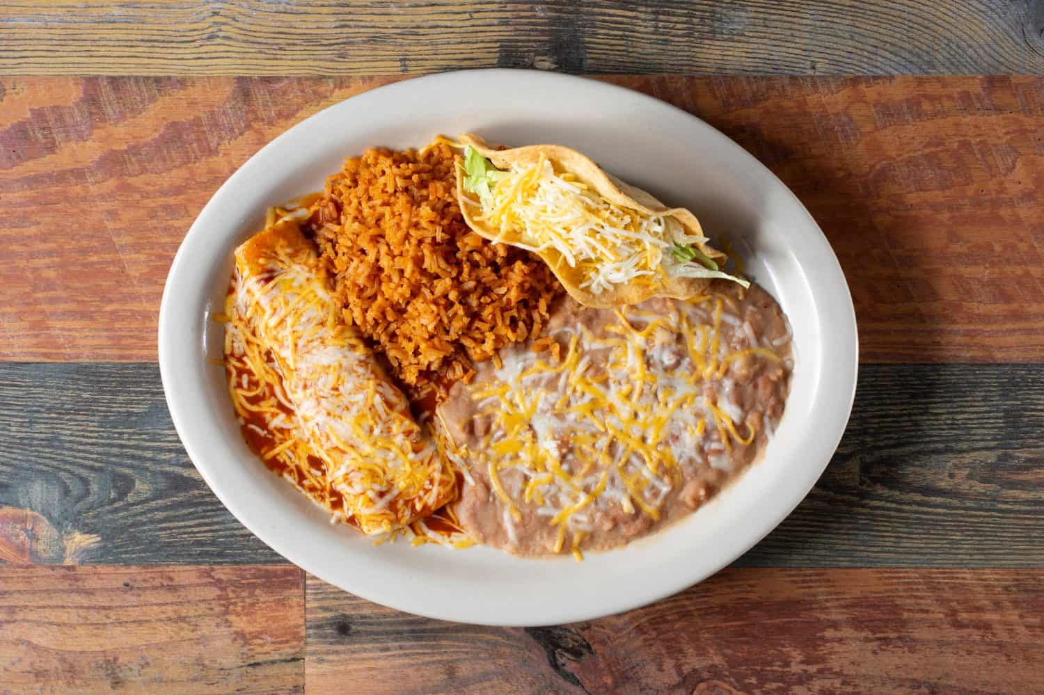A top down view of a combo plate, featuring an enchilada, hard taco, rice and beans.