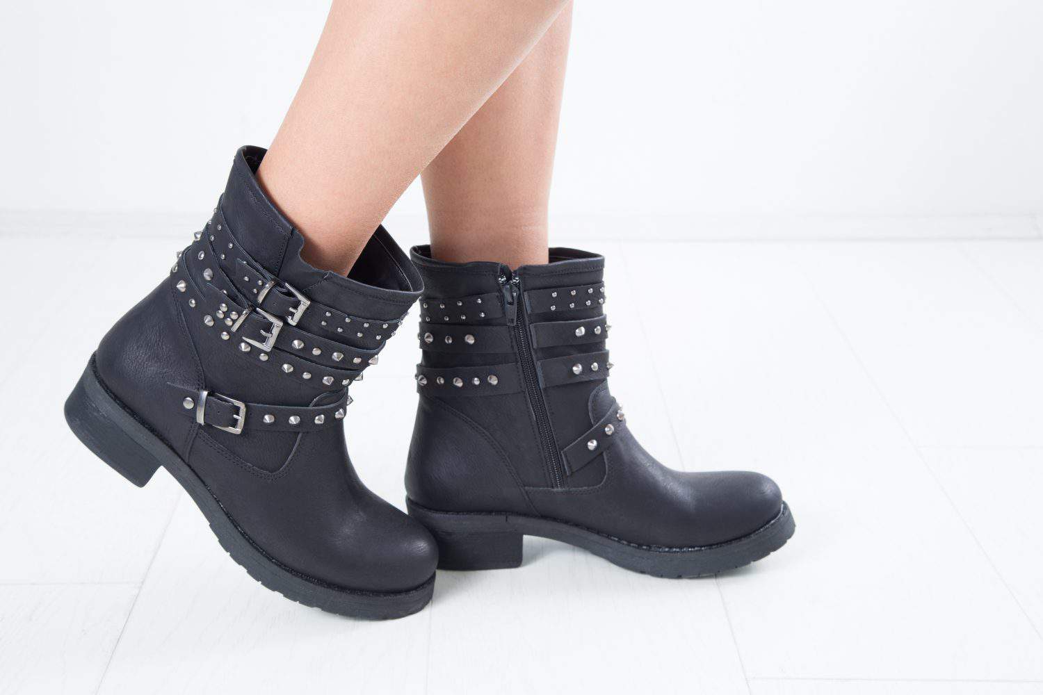 Side View Of Woman's Black Leather Ankle Boots With Straps, Metal Studs And Zipper, Studio Shot Over White Background
