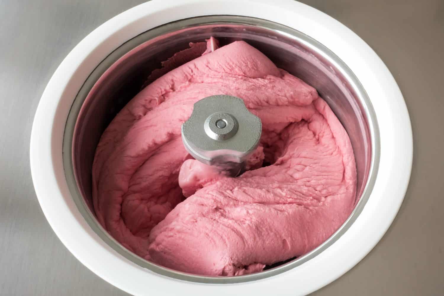 Homemade raspberry ice cream churning in a small professional ice cream machine.