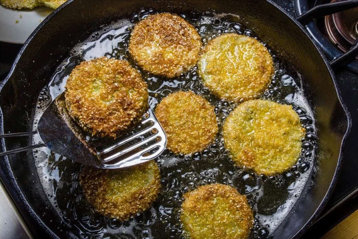 Slices of green tomato being fried to make fried green tomatoes