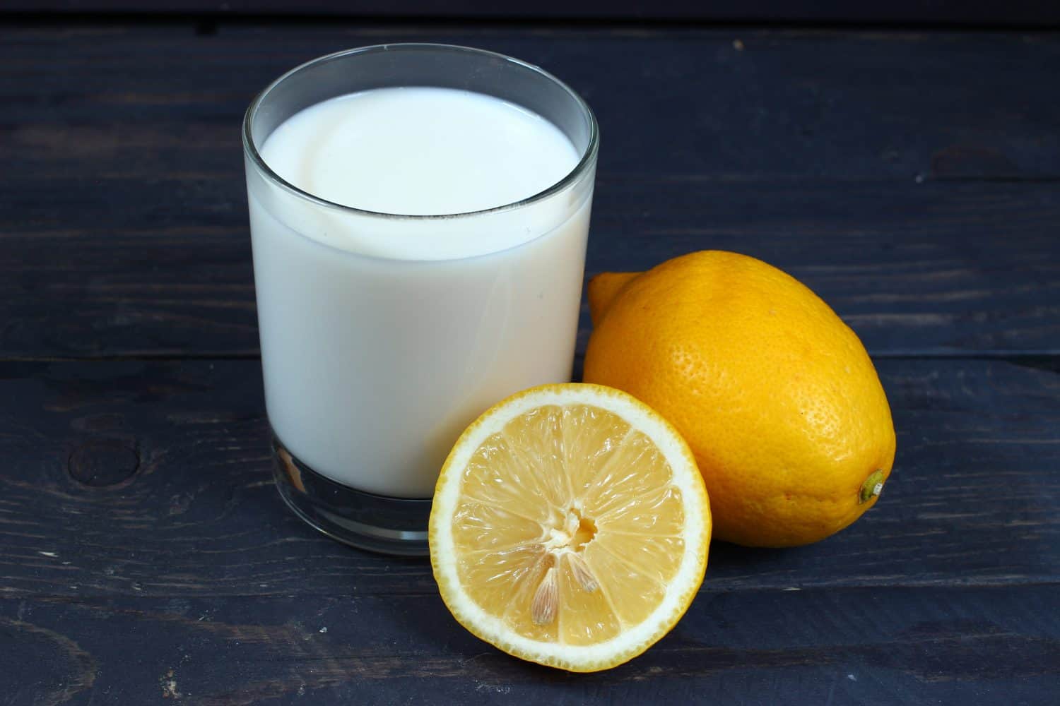 A glass of milk and lemons on a dark wooden background