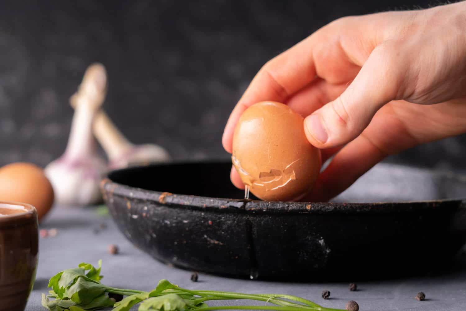 persons hand hold cracked egg and pour a yolk and protein in a frying pan to cook it, rustic style