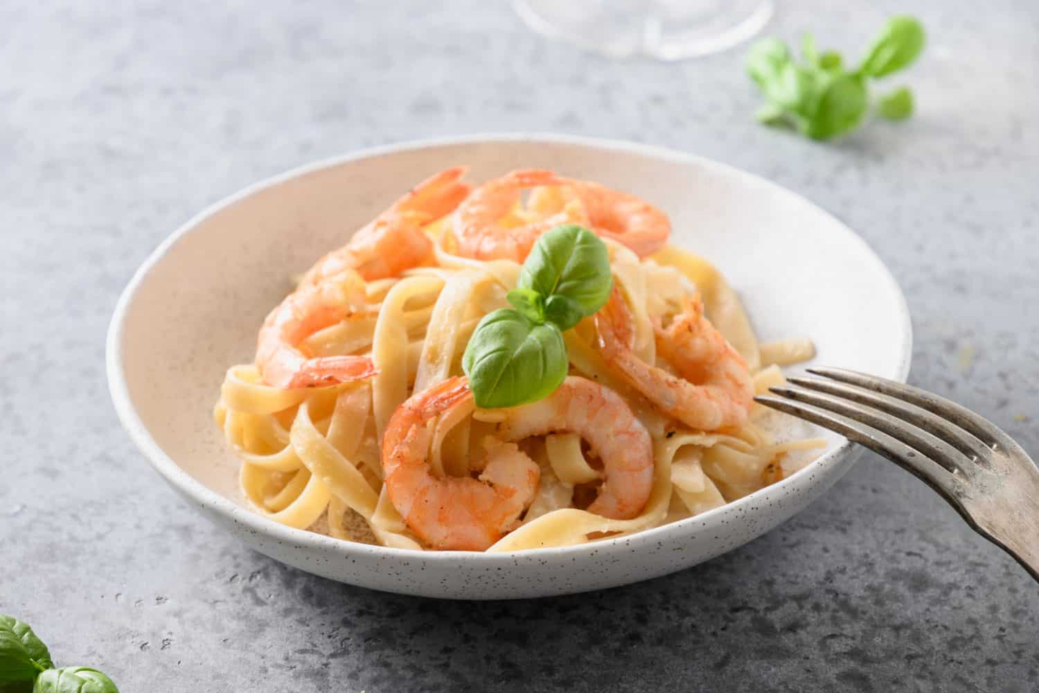 Italian pasta fettuccine with shrimps in white bowl on gray table. Close up.